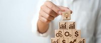 Business professional stacking wooden blocks with financial icons creating growth pyramid. Corporate strategy and success building concept for presentations.