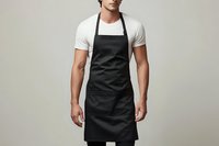Professional male chef in black apron and white t-shirt standing confidently against neutral background for culinary branding and restaurant marketing.