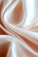 Smooth flowing curves of white and copper satin fabric create elegant abstract waves and folds against soft gradient background. Luxury design element for backgrounds.