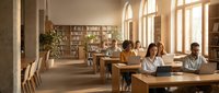 Diverse students taking exam in bright university classroom with wooden desks, bookshelves and large windows creating focused academic atmosphere.