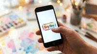 Hand holding smartphone with colorful watercolor Buy Now button on screen, mobile shopping and e-commerce concept on artistic background.