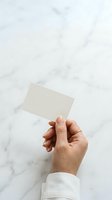 Caucasian hand holding blank cream business card against white marble background, ideal for corporate branding and professional mockup designs.
