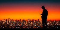 Silhouette of businessman using smartphone against vibrant sunset cityscape with bokeh lights creating atmospheric urban evening scene for technology concepts.