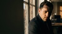 Serious businessman in dark suit looking pensively out office window during golden hour light for corporate leadership and professional success concepts.