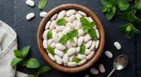 White lima beans in wooden bowl with fresh mint leaves on dark slate background for healthy cooking and nutrition concepts.