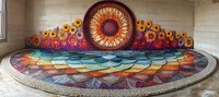 Vibrant rainbow mandala street art with sunflower motif painted on curved wall and ground, featuring geometric patterns and bright gradient colors in urban setting.
