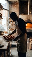 Baker holding fresh baked bread loaves in rustic brick kitchen with wood-fired oven, artisan bakery production and traditional baking craft.