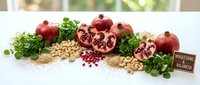Fresh pomegranates with seeds, nuts, and green herbs arranged on white surface for healthy eating and nutrition concepts.