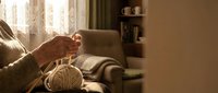 Elderly hands knitting with beige yarn ball in cozy living room, warm light, home hobby concept, relaxation and traditional craft.