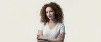 Confident young woman with curly hair and crossed arms on neutral background for business and professional marketing materials.