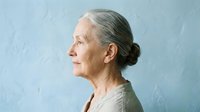 Senior woman with gray hair in profile, wearing neutral beige sweater against soft blue textured background. Mature female portrait for healthcare, wellness, aging, lifestyle content.