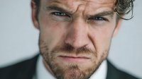 Intense close-up portrait of determined Caucasian businessman with piercing blue eyes and beard showing focused expression for corporate leadership concepts.