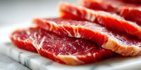 Sliced raw beef carpaccio with marbling on white marble cutting board, gourmet appetizer for restaurant menu or cooking preparation.