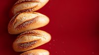 Fresh baked crusty bread rolls with poppy seeds arranged in diagonal line on dark red background, dramatic lighting creates appetizing shadows.