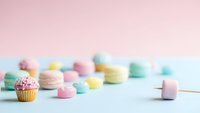 Colorful cupcake with sprinkles surrounded by pastel macarons and marshmallows on soft gradient background for sweet dessert concepts and bakery designs.