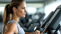 Young Caucasian woman with ponytail in gray tank top focused on treadmill display during workout at modern fitness center.