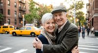 Happy senior Caucasian couple embracing on city street with yellow taxi cabs in background, showing love and togetherness in urban setting for lifestyle content.