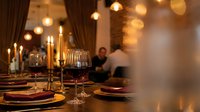 Elegant restaurant table setting with wine glasses and candles creating warm ambiance for fine dining experience with blurred guests in background.