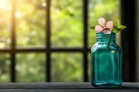 Single pink spring blossom in vintage turquoise glass jar on wooden windowsill with soft natural sunlight and blurred garden background through window panes.