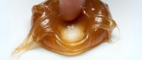 Finger pressing into stretchy amber slime with glossy, translucent texture and dripping strands for sensory play and stress relief.