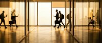 Business people silhouettes walking through modern office building lobby with large glass windows during golden hour creating professional atmosphere.