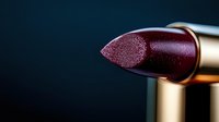 Luxurious dark burgundy lipstick with metallic shimmer close-up on black background. Golden tube holder adds elegant touch to cosmetic product photography.