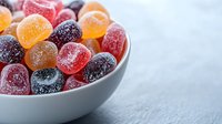 Colorful sugar coated gummy candies in white ceramic bowl on gray background. Sweet fruit jellies with crystallized sugar coating for confectionery design.