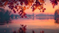 Autumn maple leaves hanging over tranquil lake at sunset with warm golden light reflecting on water surface creating peaceful seasonal landscape scene.