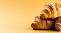 Fresh baked golden croissants with flaky layers and glossy surface against warm orange background, food photography for bakery marketing and menus.