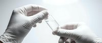 Scientist in white latex gloves holding a small glass vial with clear liquid, laboratory research and pharmaceutical testing concept.