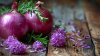 Fresh red onions with blooming purple chive flowers and green herbs scattered on rustic wooden surface, moody natural lighting creates appetizing food composition.