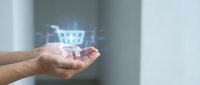 Shopping cart hologram floating above open palm of hand against blurred background, representing digital commerce, online retail, and e-commerce technology solutions.