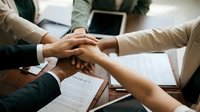 Business team joining hands together in unity over contract documents on wooden table showing teamwork collaboration and partnership agreement.