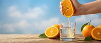 Freshly squeezed orange juice being poured into a glass with whole oranges and slices on wooden surface against blue sky, perfect for beverage, healthy lifestyle and food photography.