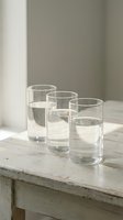 Five clear drinking glasses filled with fresh water arranged on rustic wooden table in bright minimalist interior for healthy lifestyle and hydration.