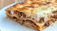 Traditional homemade lasagna with golden melted cheese and rich meat sauce layers served on white plate ready for family dinner meal.