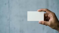 Hand holding blank white card against textured blue wall background, suitable for business card mockups, branding presentations, and corporate design templates.