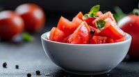 Fresh chopped red tomatoes garnished with basil leaves and peppercorns in white ceramic bowl on dark background, macro food photography for cooking blogs.