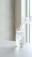Fresh water pouring from glass pitcher into tall glass on white table by window creating healthy hydration moment with natural light and bubbles.