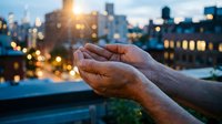 Open hands reaching toward golden sunset light over blurred city skyline with bokeh lights creating spiritual moment of hope and prayer.