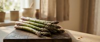 Fresh green asparagus spears on wooden cutting board in bright kitchen setting, ready for healthy cooking and meal preparation.