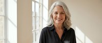 Happy mature Caucasian businesswoman with gray hair smiling confidently in modern office space with natural lighting for professional corporate content.