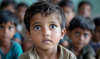 Young boy with striking eyes in classroom setting among peers, portraying innocence and curiosity in educational environment.