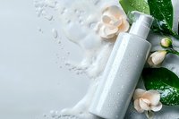 White cosmetic spray bottle with water droplets surrounded by cream roses and green leaves on wet marble surface for skincare and beauty products.