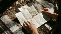 Traveler holding folded map outdoors on blanket, planning route during adventure trip or vacation journey.