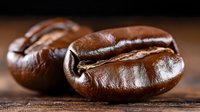 Fresh roasted coffee beans in macro shot showing rich brown color and natural texture on wooden surface, highlighting aromatic details and glossy finish.