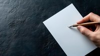 Hand holding metal pen over blank white paper on dark stone or slate background, ready for writing or creative work. Minimalist composition with copy space.