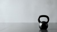 Single black kettlebell on wooden floor against white wall in minimalist gym setting for fitness and strength training workouts.