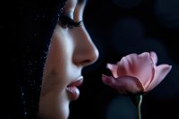 Sensual side profile of woman's face with pink rose against dark background, dramatic lighting highlights facial features and delicate flower petals.