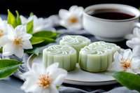 Traditional green mooncakes with jasmine flowers and tea served on white plate. Asian dessert composition with fresh blooms and dark beverage for mid autumn festival.